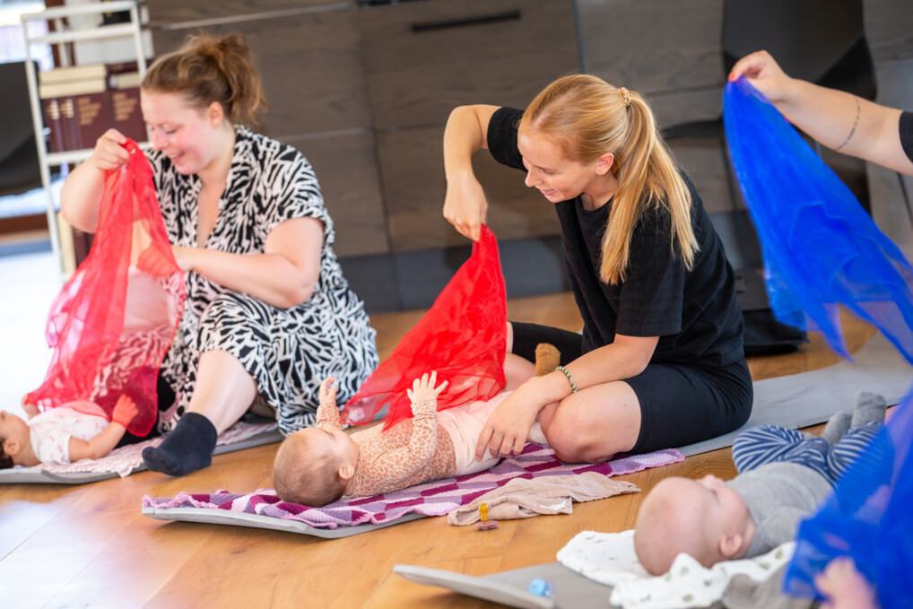 To glade babyer ligger på gulvet mens deres mødre vifter med tørklæder i forskellige farver