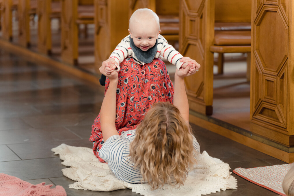 Et barn "flyver" på sin mors knæ midt på gulvet i kirken