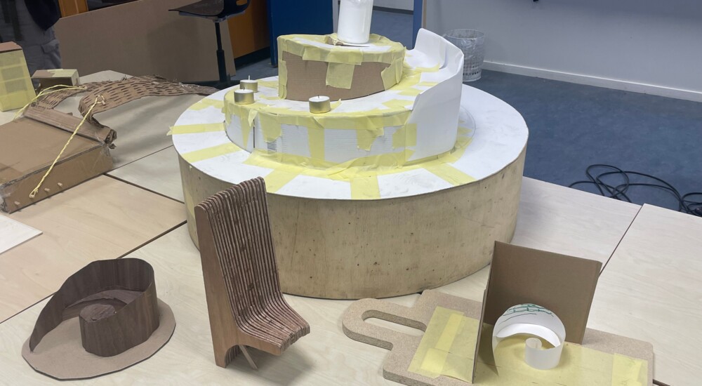 En model af et sneglehusformet religiøst rum er sat sammen af tape, bølgepap og papir på et skolebord.