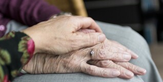 En kvindes venstre hånd ligger trøstende ovenpå en ældre kvindes hænder