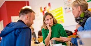 tre medarbejdere sidder omkring et skrivebord og diskuterer