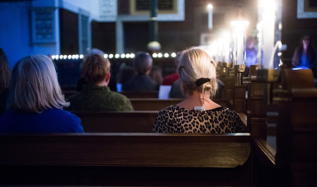 to kirkegængere sidder på en kirkebænk i oplyst med blåt lys