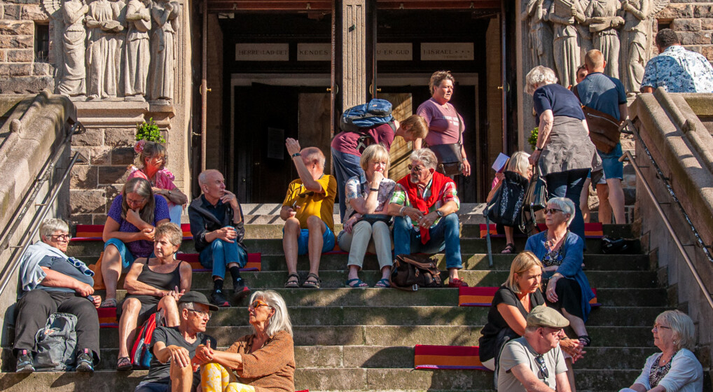 Mange mennesker i solskin siddende på kirketrappe
