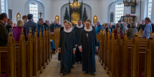 En gruppe af præster går ned ad midtergangen i St. Magleby Kirke efter en indsættelsesceremoni af kirkens nye præst