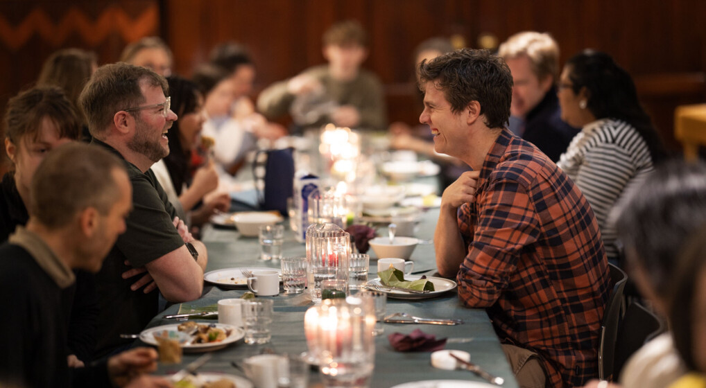 Two people sitting in front of each other, laughing at a potluck brunch table in Eliaskirken