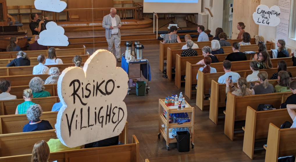 en fyldt flintholm kirke lytter til biskop peter skov-jakobsens tale bag en flaminco-sky med teksten "risikovillighed"