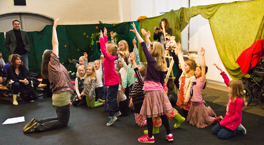 En flok børnehavebørn og en voksen leger sammen på gulvet