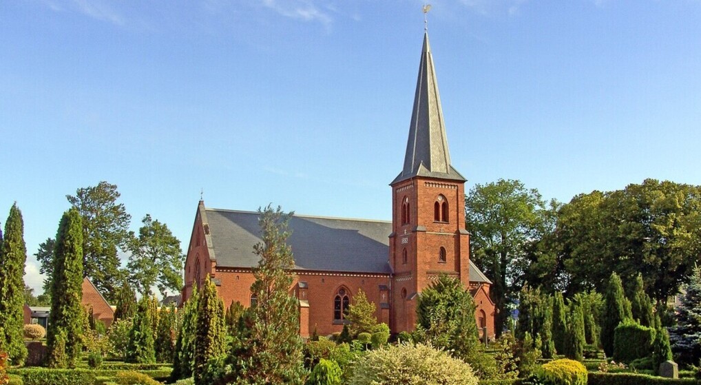 Murstenskirken i Dragør ligger omgivet af en grøn og frodig kirkegård på en sommerdag med en let blå himmel i baggrunden
