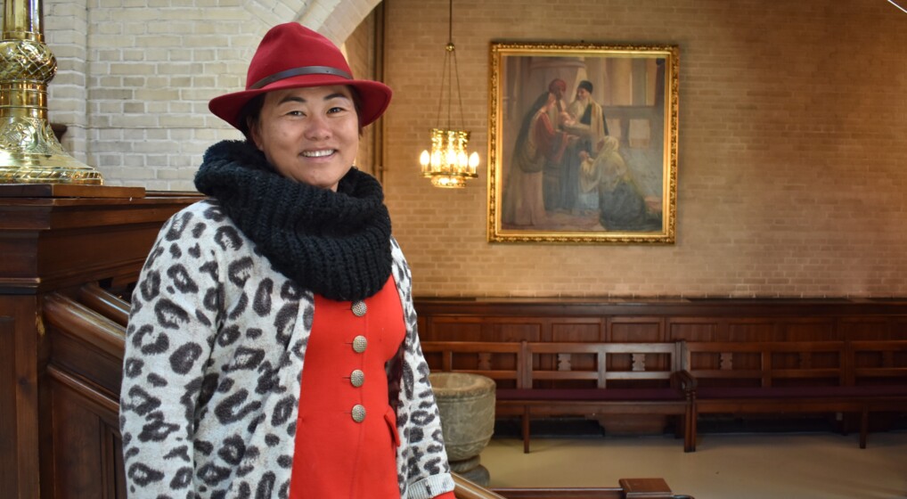 Diana stands in inside eliaskirken wearing a red hat and a big smile