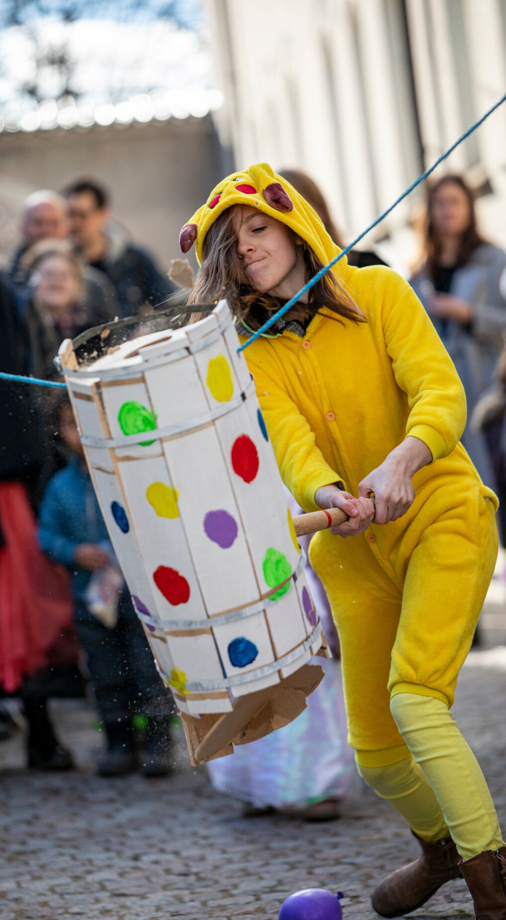 A kid dressed in a yellow Pikachu costume swings a club at a decorated barrel