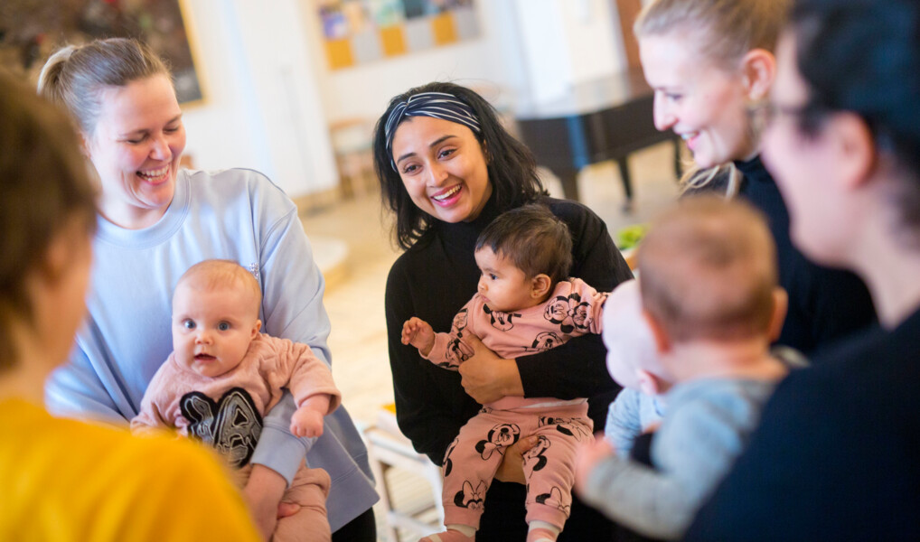  mødre med børn på armen er samlet til babysalmesqang i en kirke
