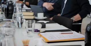 Papirer og kaffekopper på et hvidt møde bord med personer ved siden af