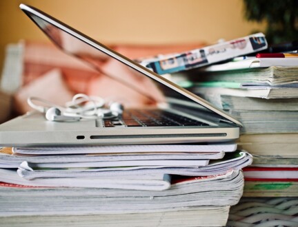 En laptop på toppen af en stak bøger og papirer