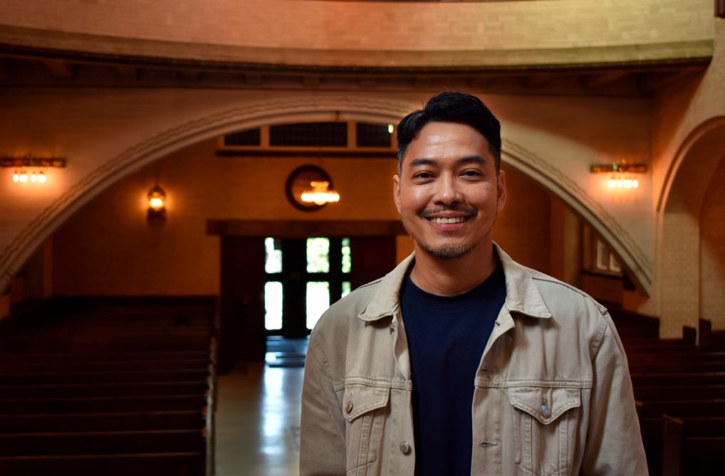 John stands inside Eliaskirken in a beige jacket and looks to the camera