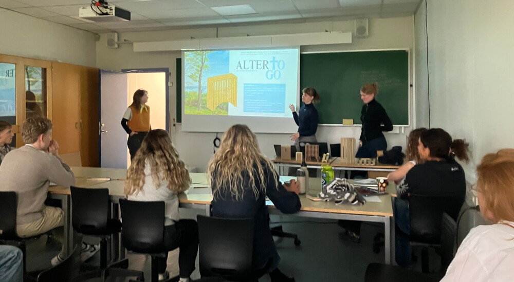 To studerende præsenterer projektet "Alter to go" foran en klasse og en underviser.