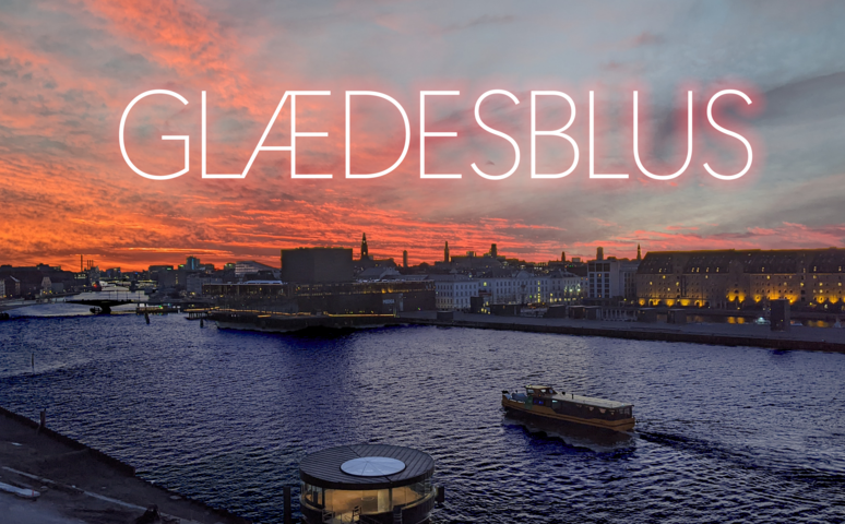 Et foto af Københavns Havn set fra Christianshavns-siden med en havnebus i rute og oplyste vinduer fra havnekantens bygninger i skumringen. Over en rødmende himmel står teksten Glædesblus med hvide bogstaver